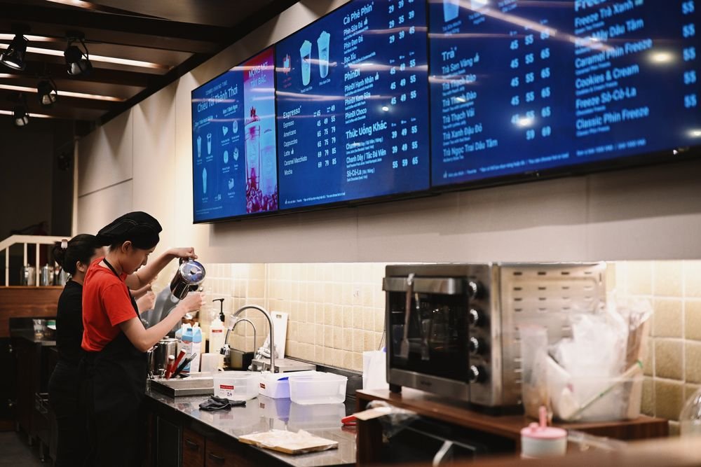 Digital menu board screens mounted above a café counter, displaying prices and drink options